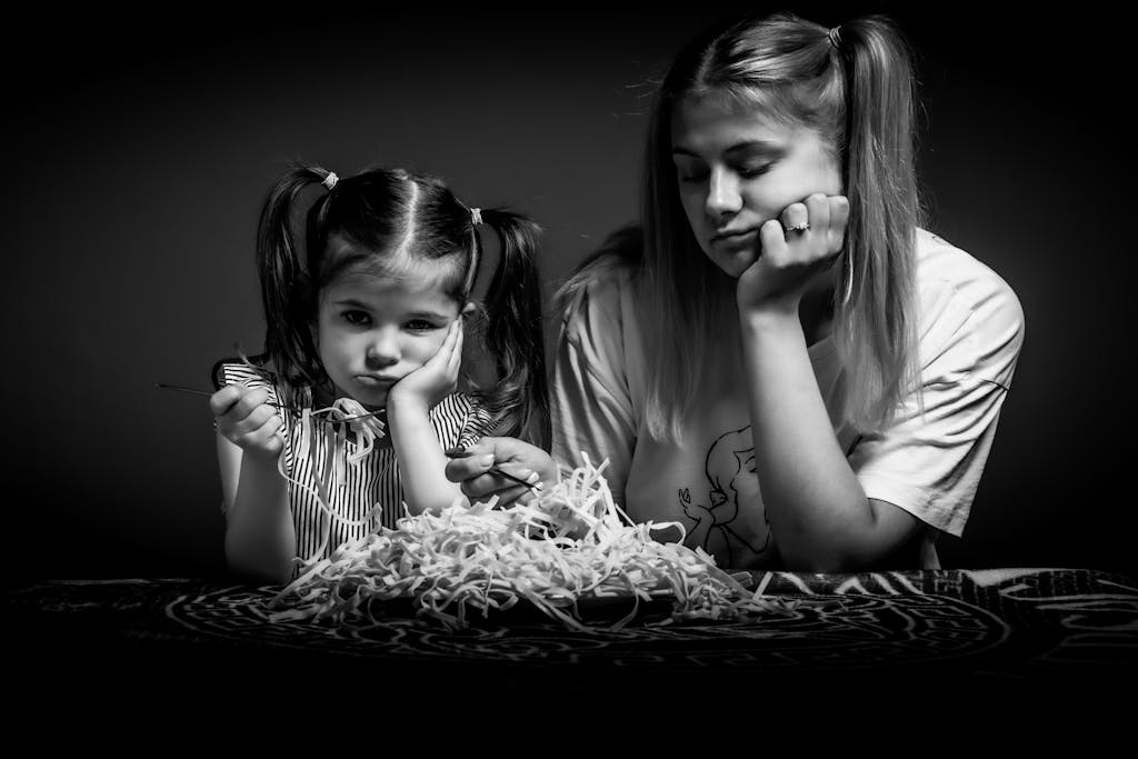 Grayscale Photo of Sisters Eating while Looking Annoyed