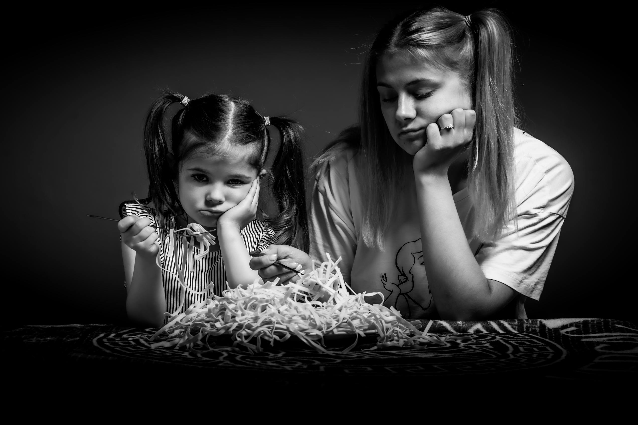 Grayscale Photo of Sisters Eating while Looking Annoyed